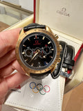 Gold Omega watch held by a hand with Olympic logo in the background