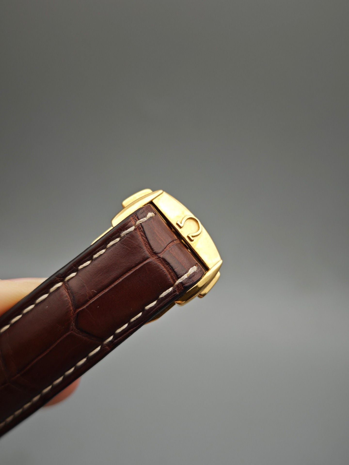 Brown leather Omega watch strap with gold buckle on a gray background
