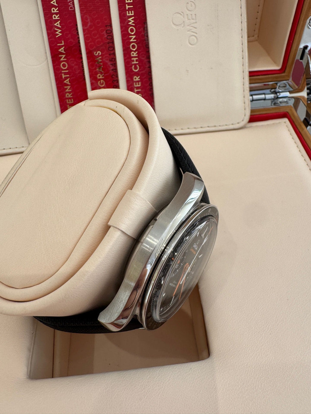 Close-up of a silver watch with a beige strap on a white surface, with an Omega box in the background.